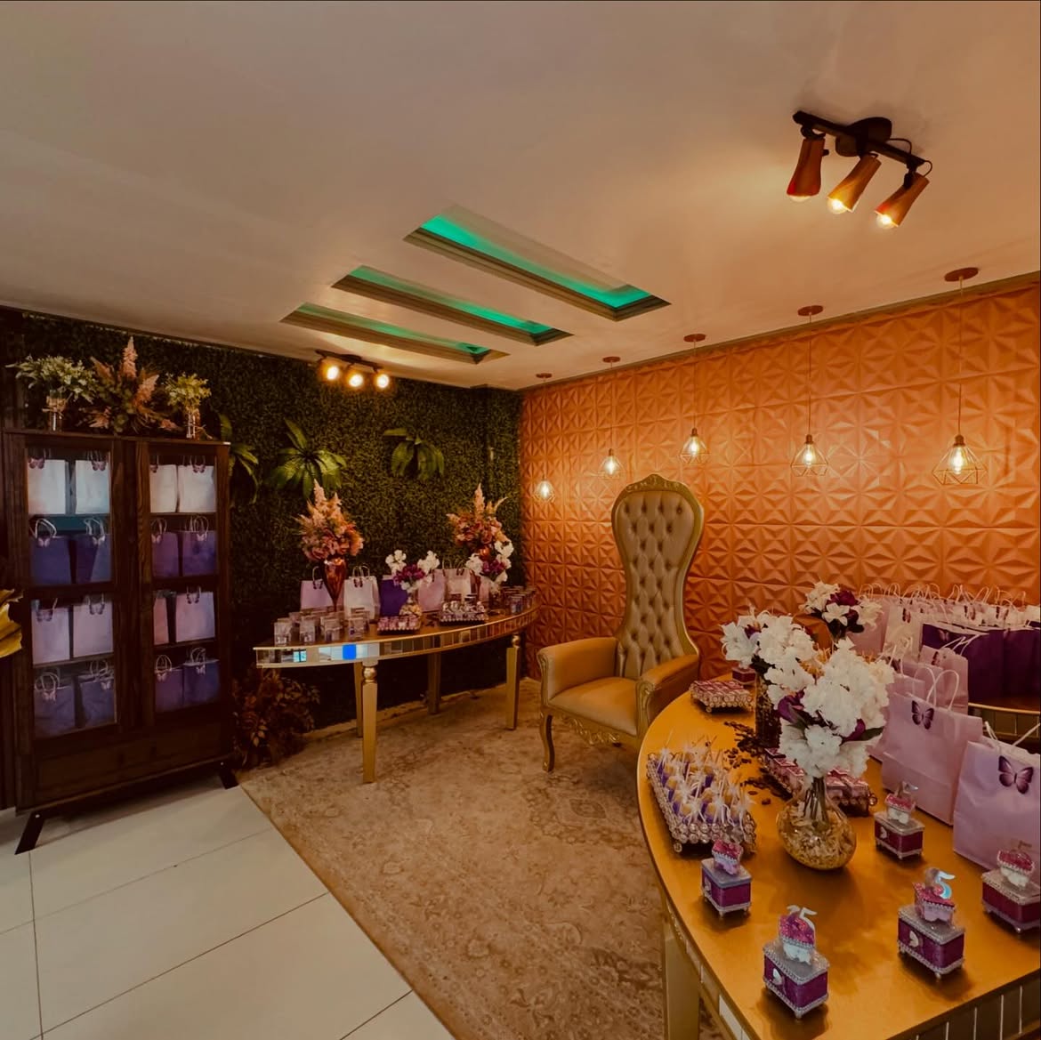Lounge real com trono dourado, parede 3D geométrica com iluminação pendente e mesa de lembranças