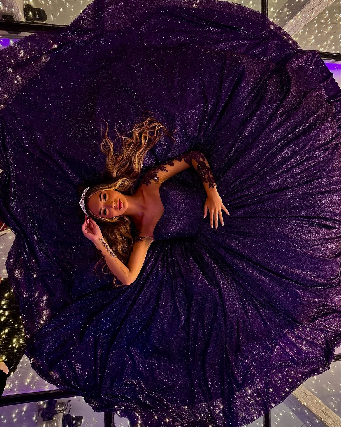 Debutante em vestido roxo brilhante com tiara sobre piso de vidro com iluminação de microlâmpadas