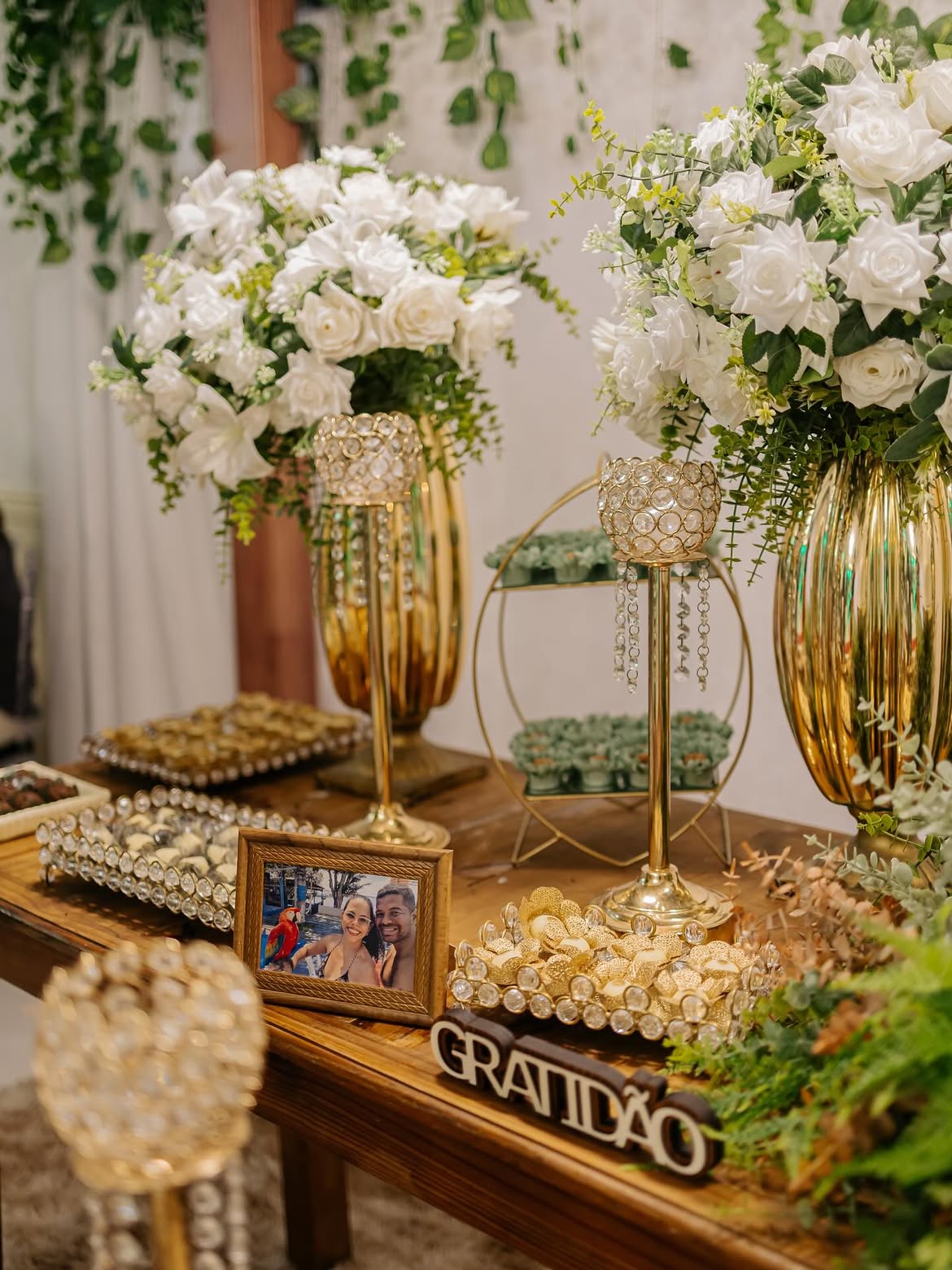 Detalhes de doces finos em forminhas douradas, rosas nobres e castiçais de cristal na mesa de casamento